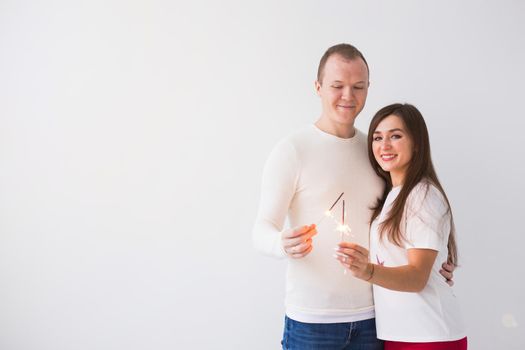 Valentine's Day concept - Young happy smiling cheerful attractive couple celebrating with glasses of champagne and sparklers on white background with copy space.