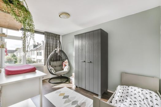 Stylish gray children's room with a wooden crib, a comfortable chair and a white table
