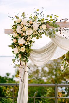 Fragment of a wedding arch decorated with tea roses, green leaves, branches and white cloth. High quality photo