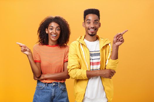 Which one telling true. Joyful and friendly good-looking couple, african american woman pointing left and dark-skinned guy right smiling broadly at camera giving advices but disagree with each other.