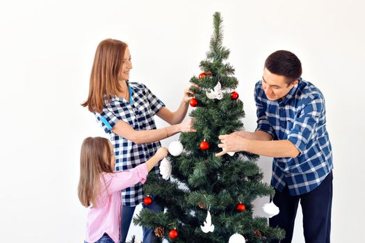 Holidays, parents and celebrating concept - Happy family decorating a Christmas tree with baubles in the living-room on white background.