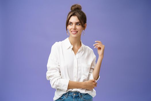 Feminine and stylish modern charming girl with gapped teeth and pimple posing in trendy white blouse and round earrings gazing left charmed and sensual with cute smile over purple background. Lifestyle.
