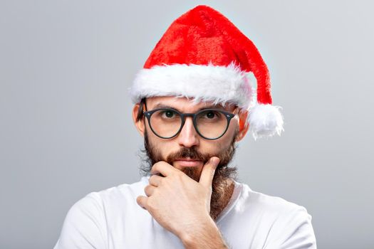 Holidays and people concept - Portrait of a handsome brutal man in Christmas hat. Over grey background