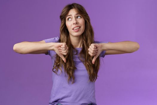 Unimpressed ignorant snobbish attractive curly-haired girl disagree lame idea look away disappointed show thumbs down dislike disapproval gesture not interested upset purple background.