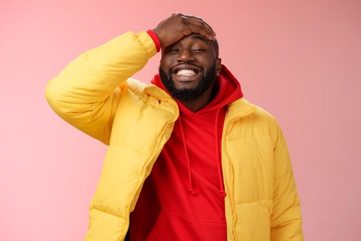 Charming cute black bearded 25s guy forget something stupid silly smiling friendly punch forehead grinning feel awkward say sorry standing pink background joyfully relaxed. Copy space