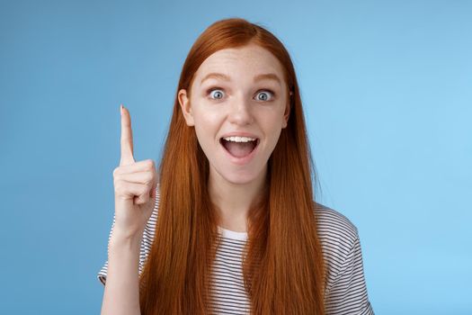 Excited good-looking cheerful ginger girlfriend add idea conversation raise index finger eureka gesture open mouth wide tell suggestion smiling broadly pondering excellent variant, blue background.