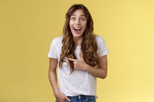 Joyful charismatic woman having fun chatting friend have funny amusing conversation discuss comedy movie pointing left fascinated impressed open mouth smiling broadly laughing yellow background.