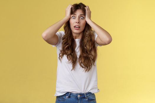 Troubled concerned anxious panicking woman female employee lose control grab head nervously stare camera frustrated scared gasping hopeless puzzled standing yellow background.