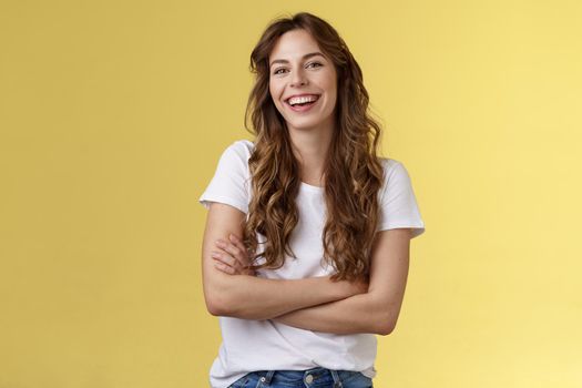 Entertain me. Friendly charismatic female long curly haircut laughing joyfully hang out friends cross arms chest feel chilly slightly cold have amusing pleasant conversation yellow background.