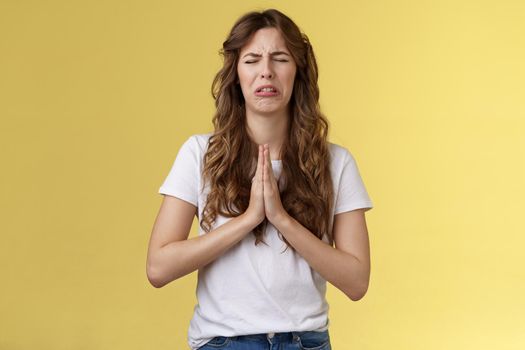 Please beg you. Sobbing timid insecure distressed cute whining girl crying upset close eyes grimacing hold hands pray pleading asking favour apologizing sincere hope for pity yellow background.