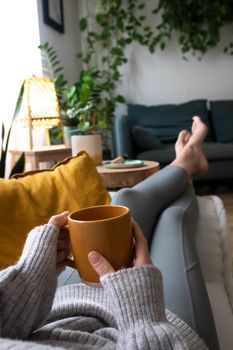 POV of young woman relaxing at home with cup of tea lying on sofa. Vertical. Lifestyle concept.