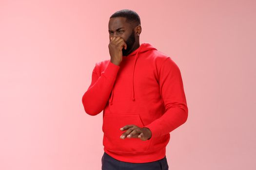 Intense bothered african american man feel unwell close nose cringe dislike aversion wanna puke smell terrible reek, disgusting stink, expressing disgust look junk, standing pink background.