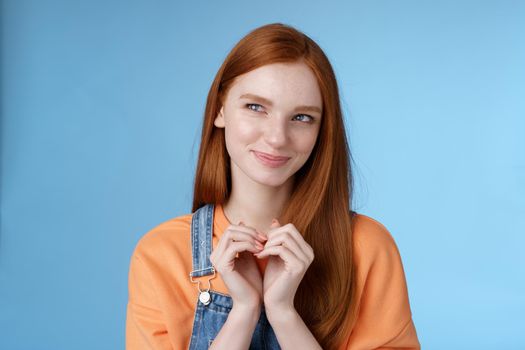 Devious tricky young girl have excellent plan smirking delighted mysteriously look upper left corner smiling have idea thoughtfully twiddles fingers standing rejoicing blue background.