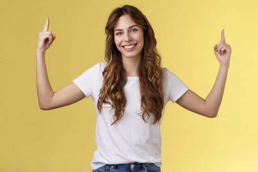 Friendly charismatic good-looking woman showing you great promo place pointing up index fingers raised top copy space smiling toothy delighted tilt head introduce advertisement great choice. Lifestyle.