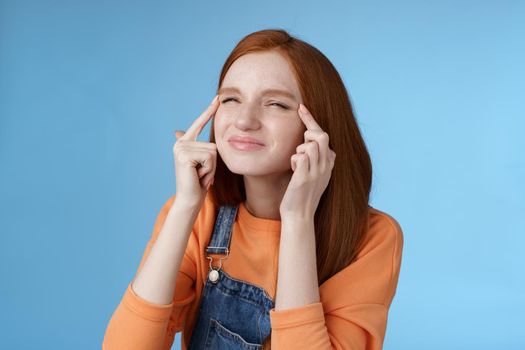 Cute funny european redhead girl forgot glasses trying read sigh stretch eyelids squinting frowning focused look upper left corner perplexed see what happening, standing blue background.