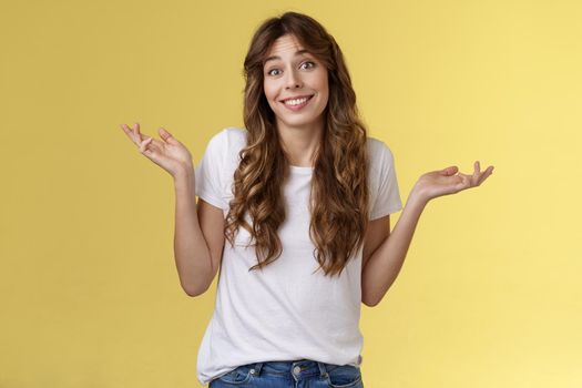 Who cares have fun. Carefree indifferent outgoing happy young woman shrugs raise hands sideways clueless unbothered apathic to topic uninterested smiling broadly careless yellow background.