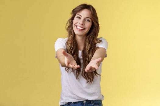 Come closer take my hand. Cheerful lovely charismatic tender woman extend arms forward camera wanna hold receive charming gift tilt head smiling pleased grateful stand yellow background. Copy space