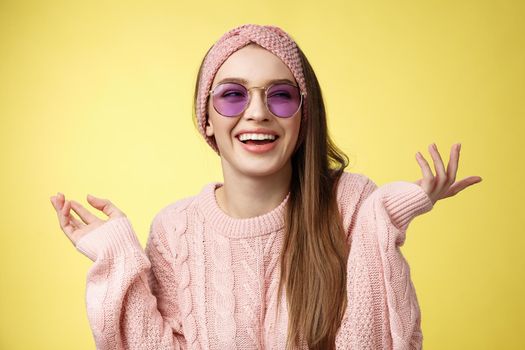 Cute glamour satisfied carefree female tourist getting ready sea vacation wearing trendy sunglasses spread hands sideways looking aside smiling delighted, enjoying vacation over yellow background.