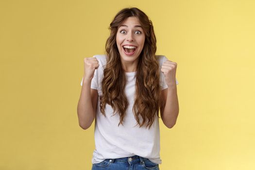 Cheerful supportive happy female fun fist pump relieved triumphing cheering rooting for favorite team winning smiling broadly hopefully look camera celebrating victory yellow background.