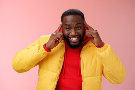 Think about it. Portrait charming creative young happy african guy bearded hold index fingers temples brain smiling broadly share awesome idea great thought, grinning silly standing pink background.