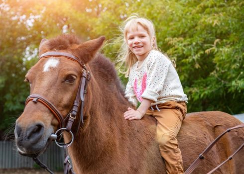 portrait of laugh happy little girl riding a horse bareback