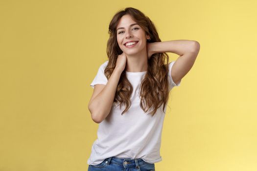 Cheerful charismatic good-looking curly-haired woman stretching posing yellow background touch neck flirty smiling relaxing perfect summer vacation booking weekend trip finally rest under sun. Lifestyle.