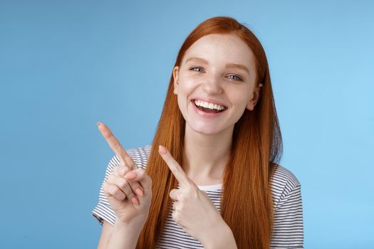 Happy carefree smiling redhead caucasian girl ginger straight hairstyle pointing upper left corner laughing joyfully amused cool promo giving recommendation try new product, standing blue background.