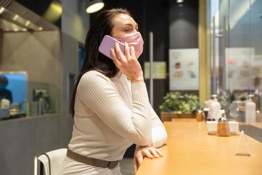 woman in mask speaking by phone sitting in cafe public place