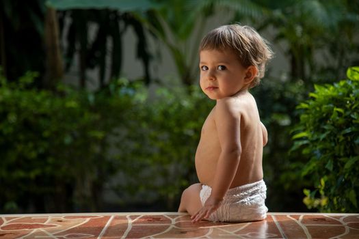 adorable little baby sitting on terrase outdoors summer sunny day rear view