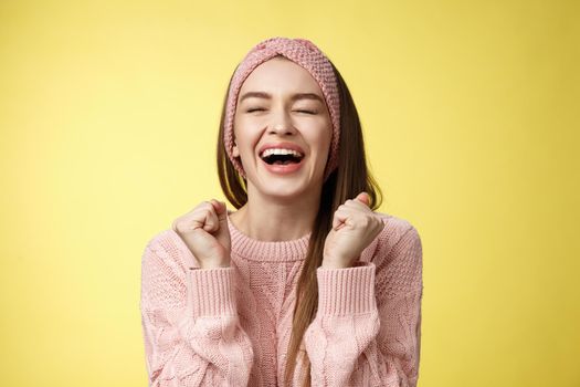 Relieved happy triumphing attractive european woman wearing pink knitted sweater yelling yes satisfied, raising fists in victory close eyes smiling, celebrating win, feeling lucky hearing good news.