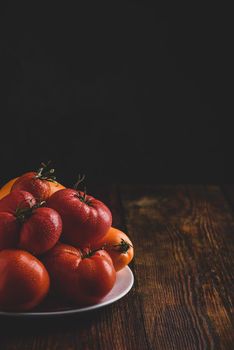 Fresh red and yellow tomatoes on white plate over wooden surface