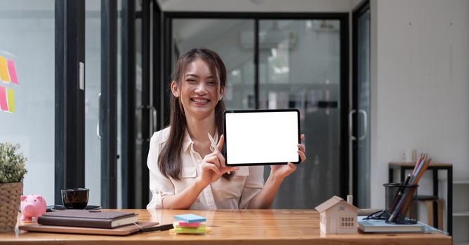 Portrait of Asian woman showing or presenting tablet computer with blank white screen, real estate working at office.