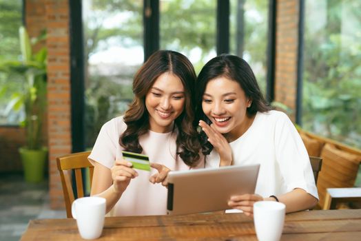 Happy relaxed young female friends doing online shopping through laptop and credit card in living room