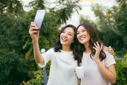 Lifestyle of Two beautiful Happiness Long Hair Women are  Using Mobile Phone for Selfie in Garden. Asian Female Models Portrait Concept.