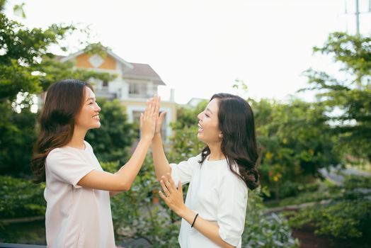 Two beautiful young women giving high five - Pretty girls standing on outdoors and having fun - Best girlfriends making a promise