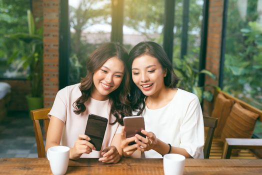 Two happy friends watching media content in a tablet sitting in a table at home