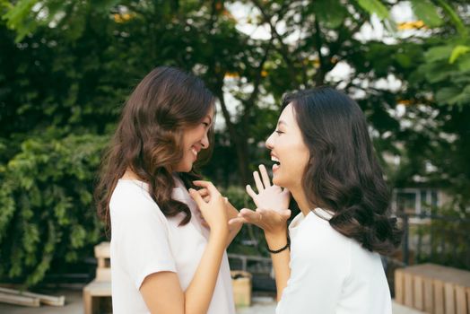 Beauties in style. Two beautiful young well-dressed women smiling at camera while standing embracing outdoors