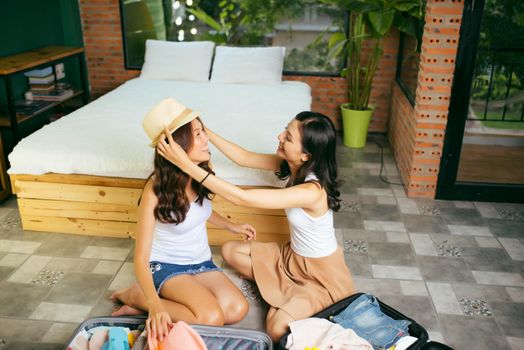 Two happy young women while packing suitcases at home for vacation or trip