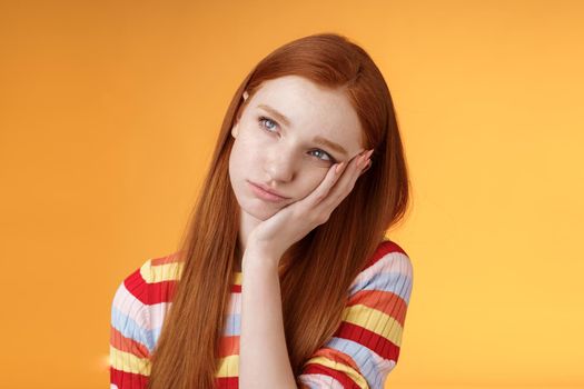 Lonely upset moody cute redhead girlfriend feeling boredom leaning palm look up pouting frowning displeased standing uneasy attend boring meeting, staring uninterested reluctant orange background.