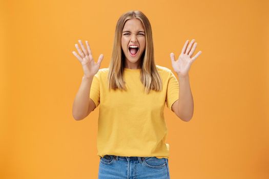 Woman releasing stress yelling with joy and pleasure gesturing with raised arms being daring and rebellious not afraid to show emotions standing passionate and expressive against orange background. Body language concept