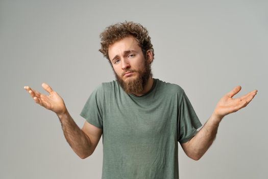Handsome man with curly hair showing I don't know gesture with both hands isolated on white background. Portrait of confused young man on white background.