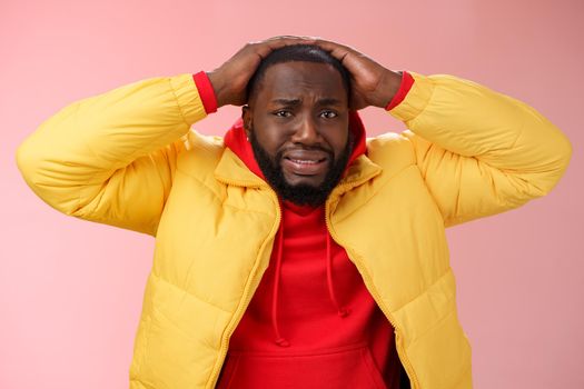 Troubled shocked young upset male coworker feel bad anxiously cringing holding hands head frowning losing bet lottery standing sorrow unhappy pink background wear yellow coat. Copy space