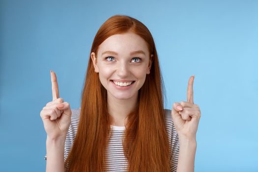 Cheerful curious amused happy entertained redhead pretty girl gazing pointing up smiling approval like interesting product watching perfomance enjoy cool holiday promos, standing blue background.