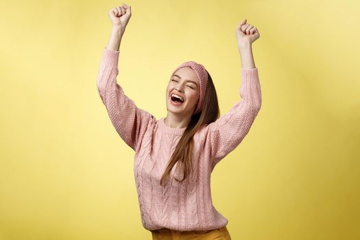 Positive celebating happy european young woman wearing casual sweater yelling happily shouting yes, triumphing racing hands up in success jumping ecstatic rejoicing cheerfully over success. Copy space