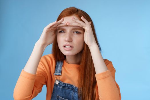 Worried clingy redhead girlfriend spying boyfriend peer from distance squinting focus sight look afar hold hands forehead cover eyes sunlight standing concentrated blue background.