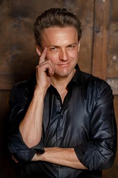 Stylish Blonde Man in Sexy Black Shirt Posing and Looking at Camera Isolated on Wood Background. Wood Background. High quality photo