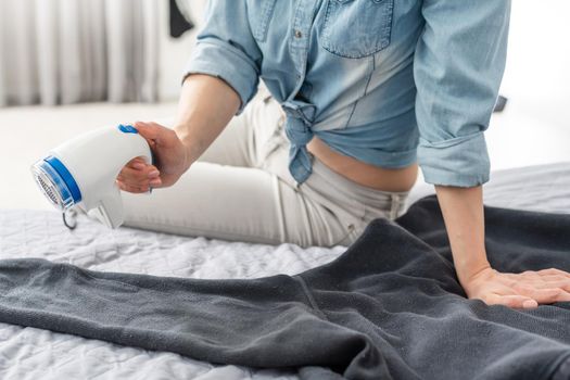 Wireless device for cleaning knitted fabrics from lint. The woman is removing the lint from the sweater