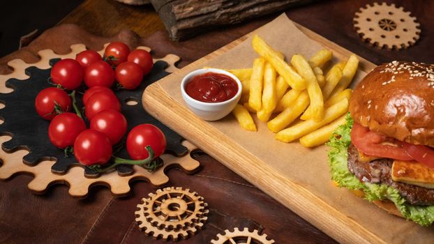 Tasty beef burger and french fries with a cherry tomatoes served on a decorative wooden part of a simple mechanism. Street food concept. Fast food concept. Restaurant concept.