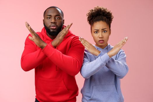 Nervous displeased two african-american man woman asking friend tell they absent not here show cross signs frowning disturbed worried begging not tell quit, stop standing pink background.