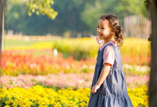 Little Asian girl with pink magnifying glass turn back and smile stand in front of flower garden with morning light.